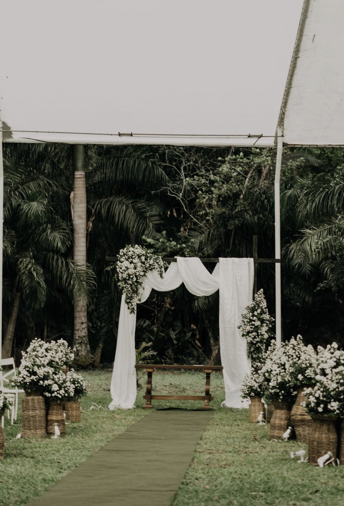 Altar de casamento com véu branco e flores na grama, cercado pela mata