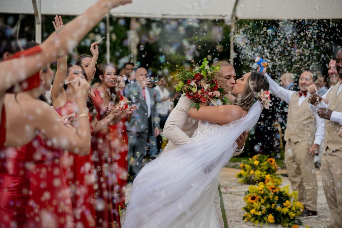 Casal de noivos se beijando sob chuva de confete, cercado pelos convidados